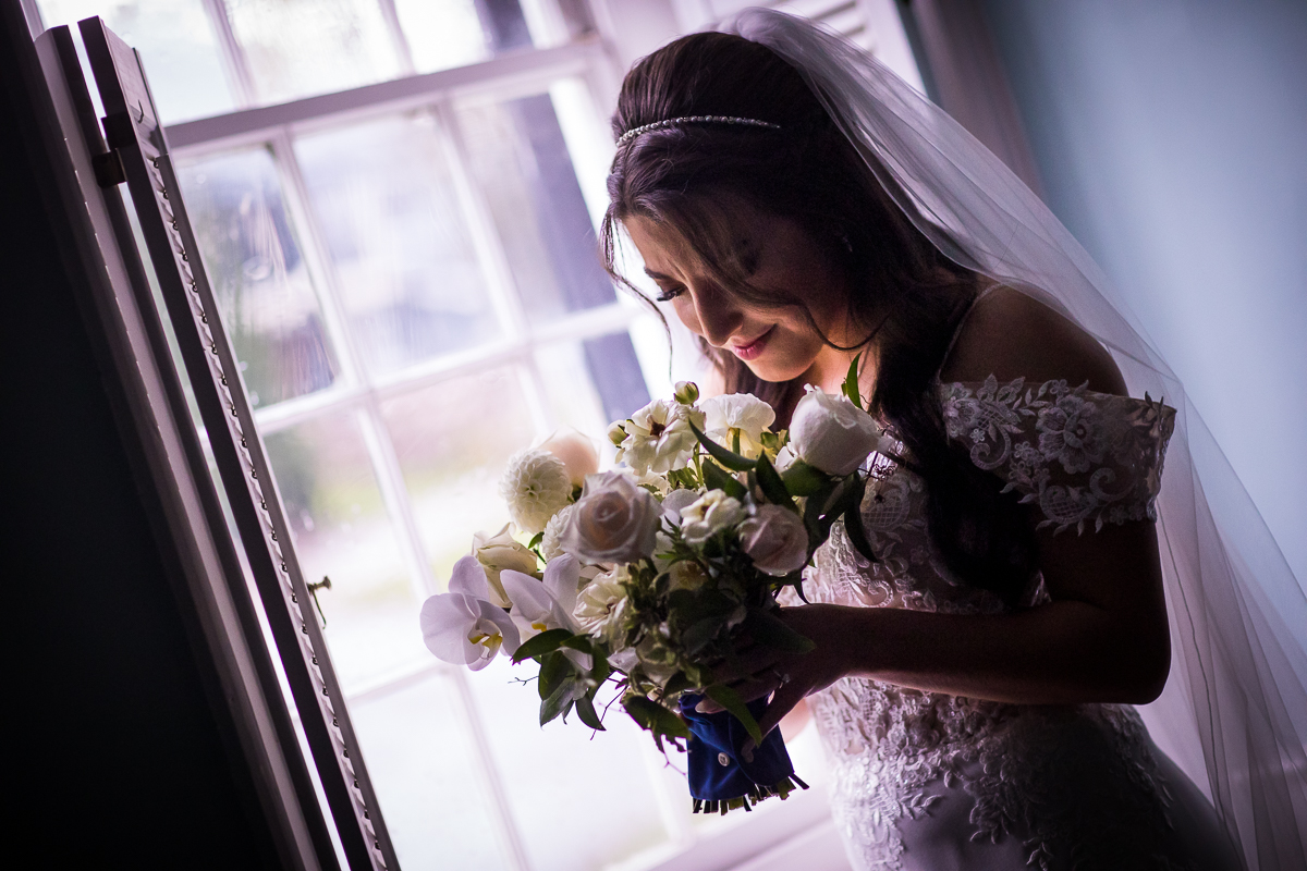 bride looking down at bouquet smiling in front of window in bridal suite