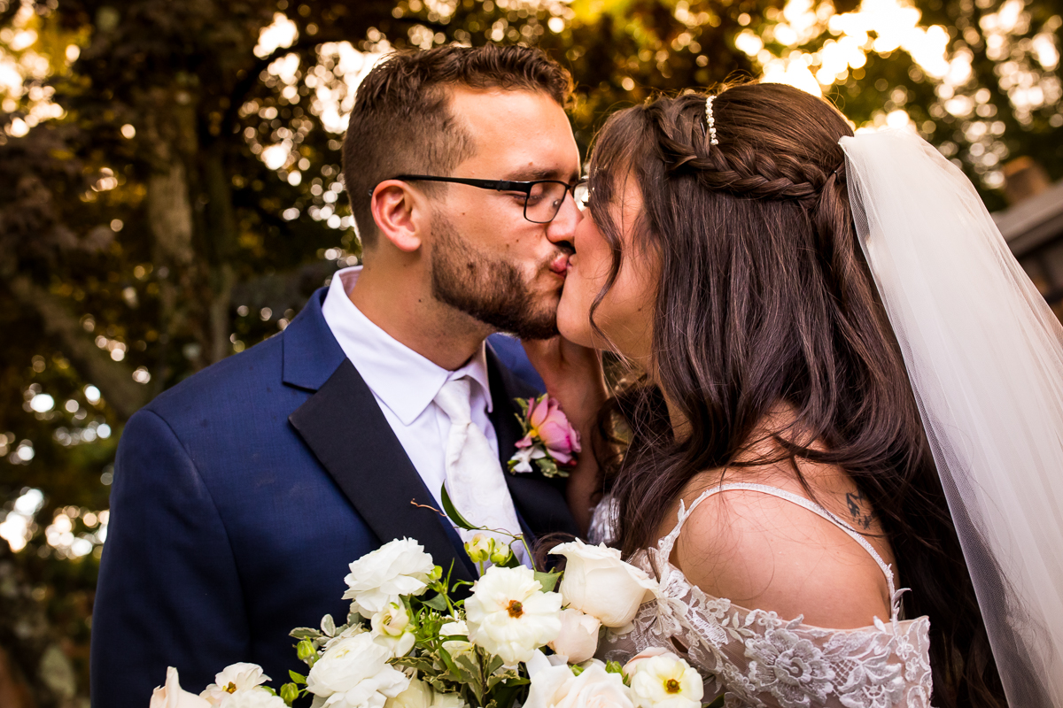 bride and groom kissing with golden hour light behind them during wedding portraits