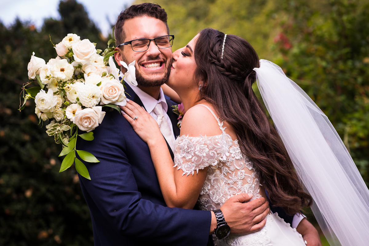 bride kissing groom on cheek holding white flower bouquet outside allenberry resort wedding