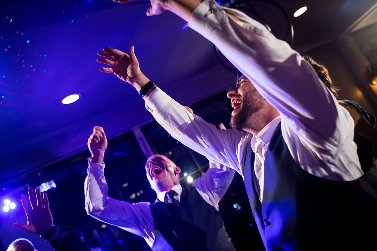 groom and groomsman dancing and singing with colorful lights around during wedding reception