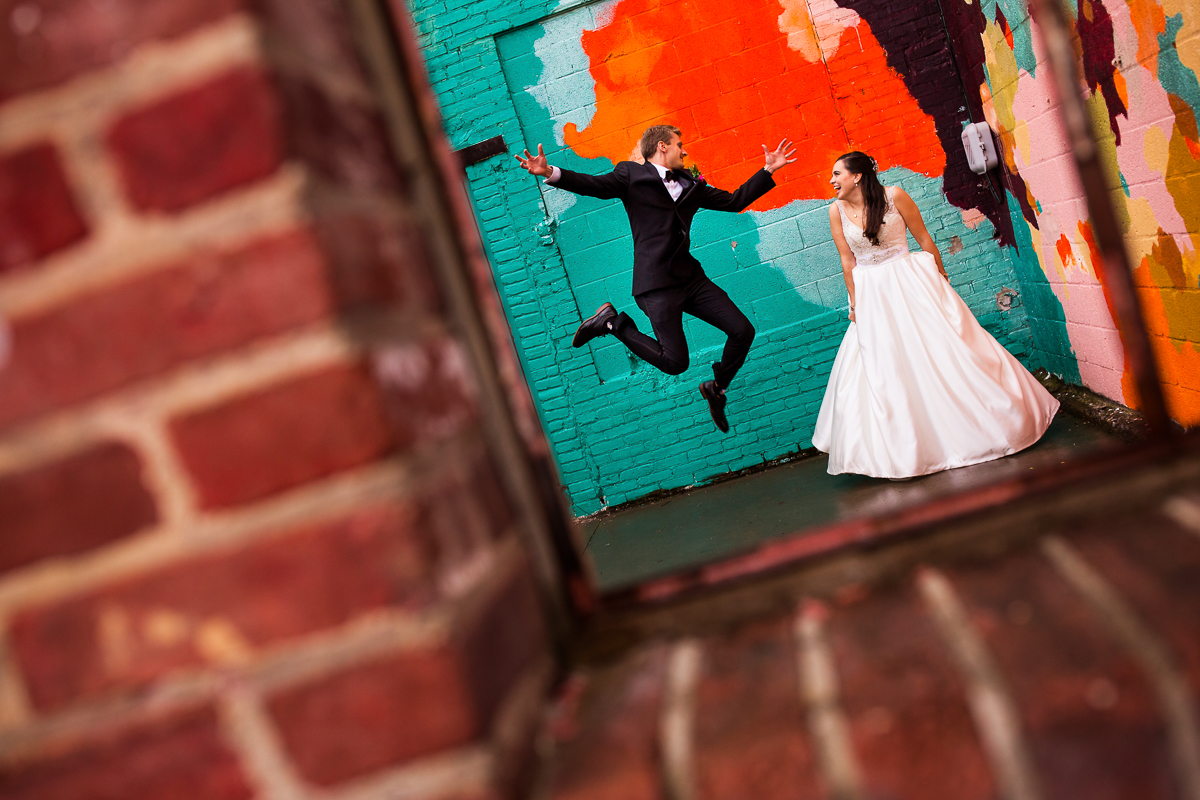 fun bride and groom wedding portraits groom jumping in front of mural while bride laughs the bond wedding photographer 