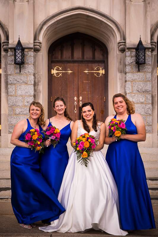 bride and bridesmaids posing in front of church wearing blue dresses and colorful bouquets central pa wedding photographer