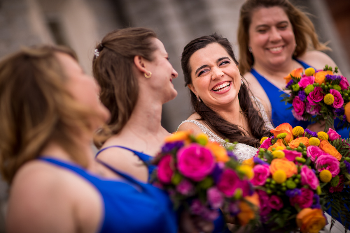 bride smiling and laughing with bridesmaids wearing cobalt dresses and holding colorful bouquets