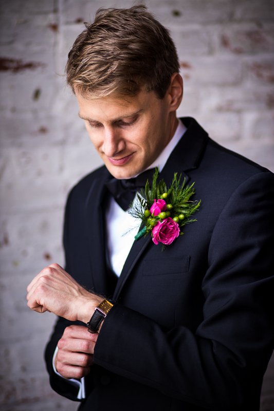 groom fixing watch during getting ready photos in front of exposed brick wall 