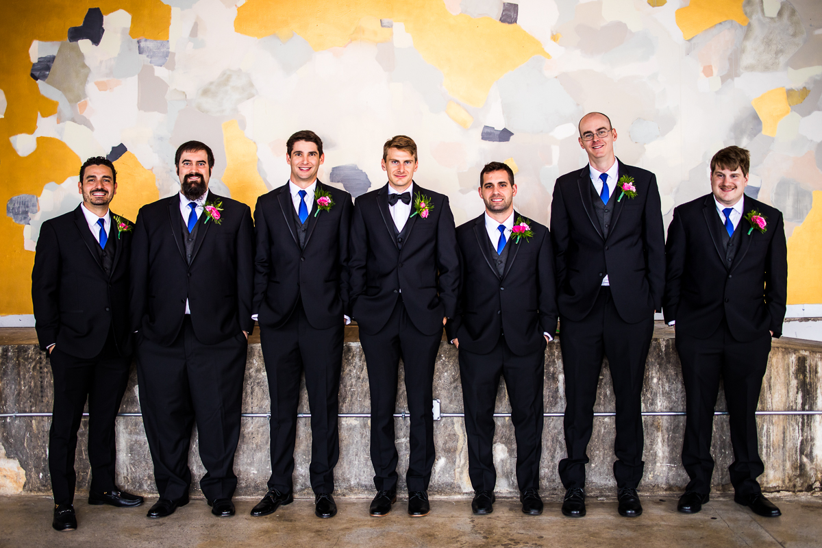 groom and groomsman standing in front of mural wall smiling 