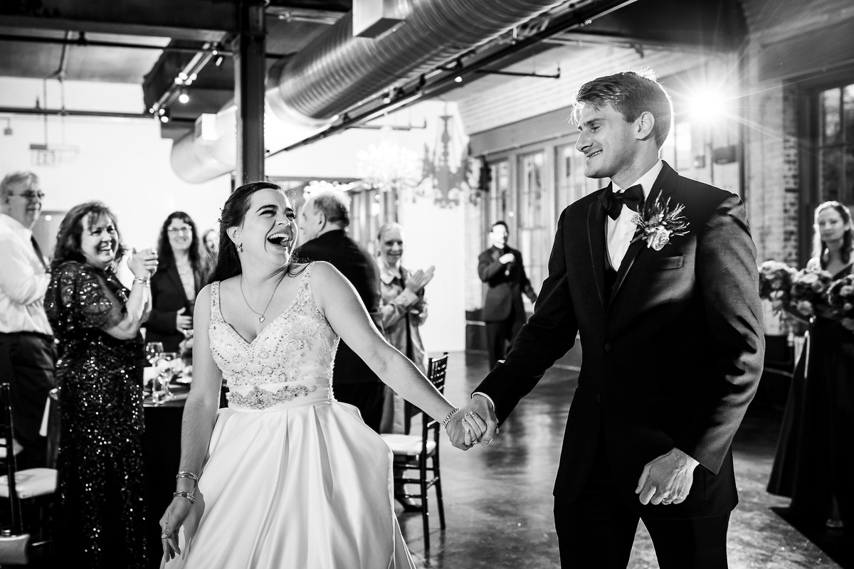 black and white photo of bride and groom entering into wedding reception smiling and looking at each other 