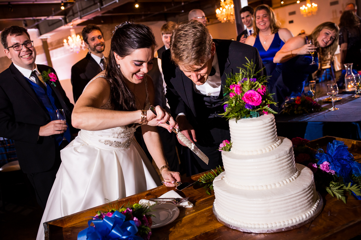 bride and groom cutting white cake with colorful flowers on top during the bond wedding reception