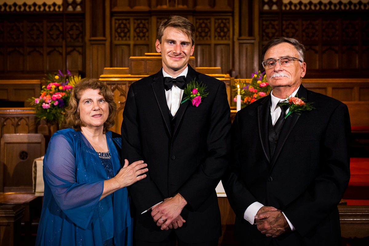 groom smiling posing with parents during family photos