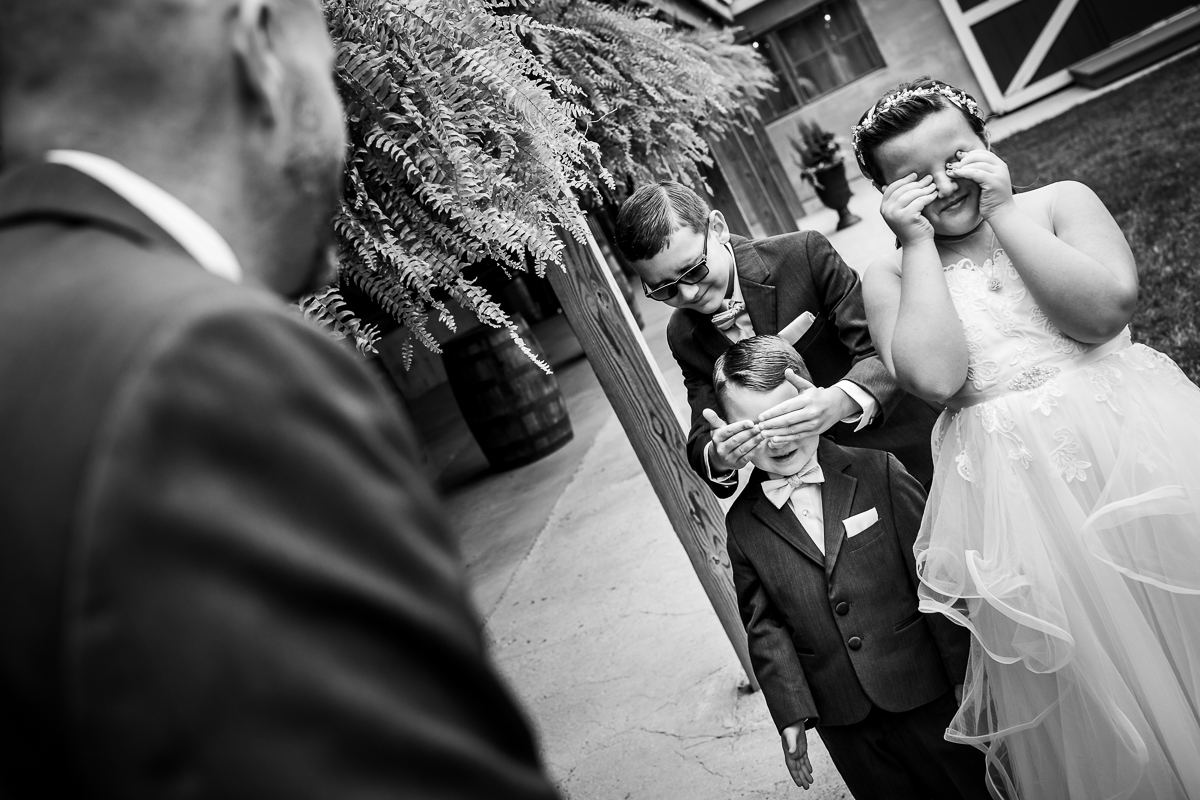 black and white photo of kids covering eyes before seeing dad during first look candid authentic heritage restored wedding photographer