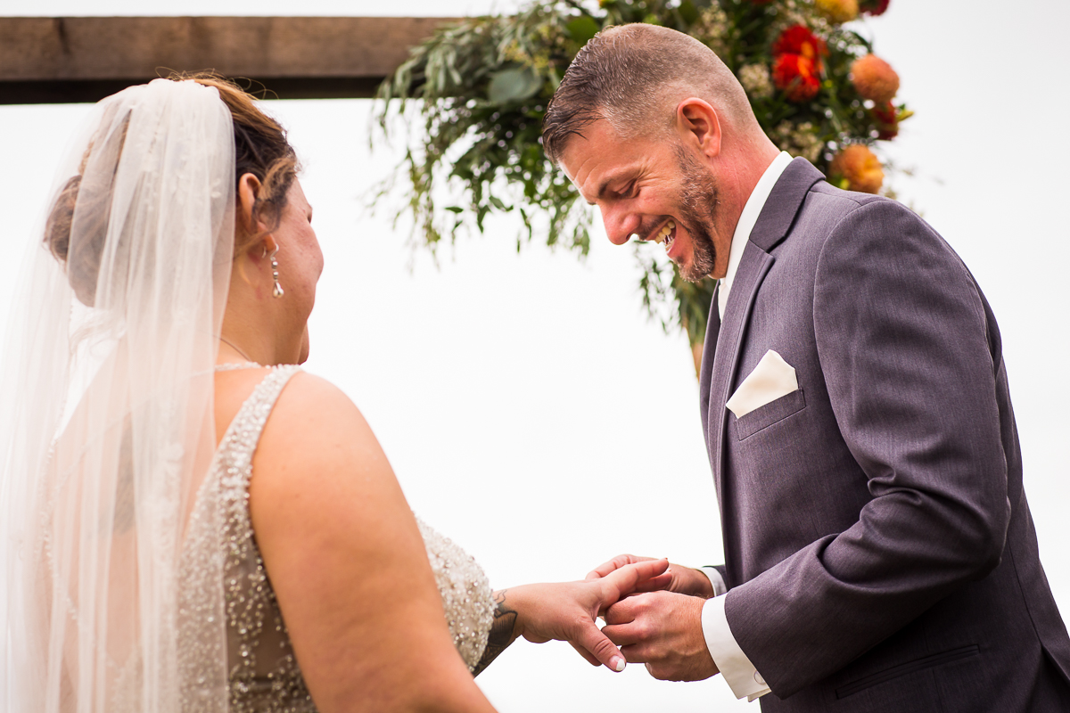 groom smiling laughing putting ring on bride's finger