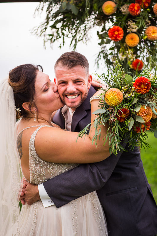 heritage restored wedding photographer bride giving groom kiss on cheek holding bouquet 