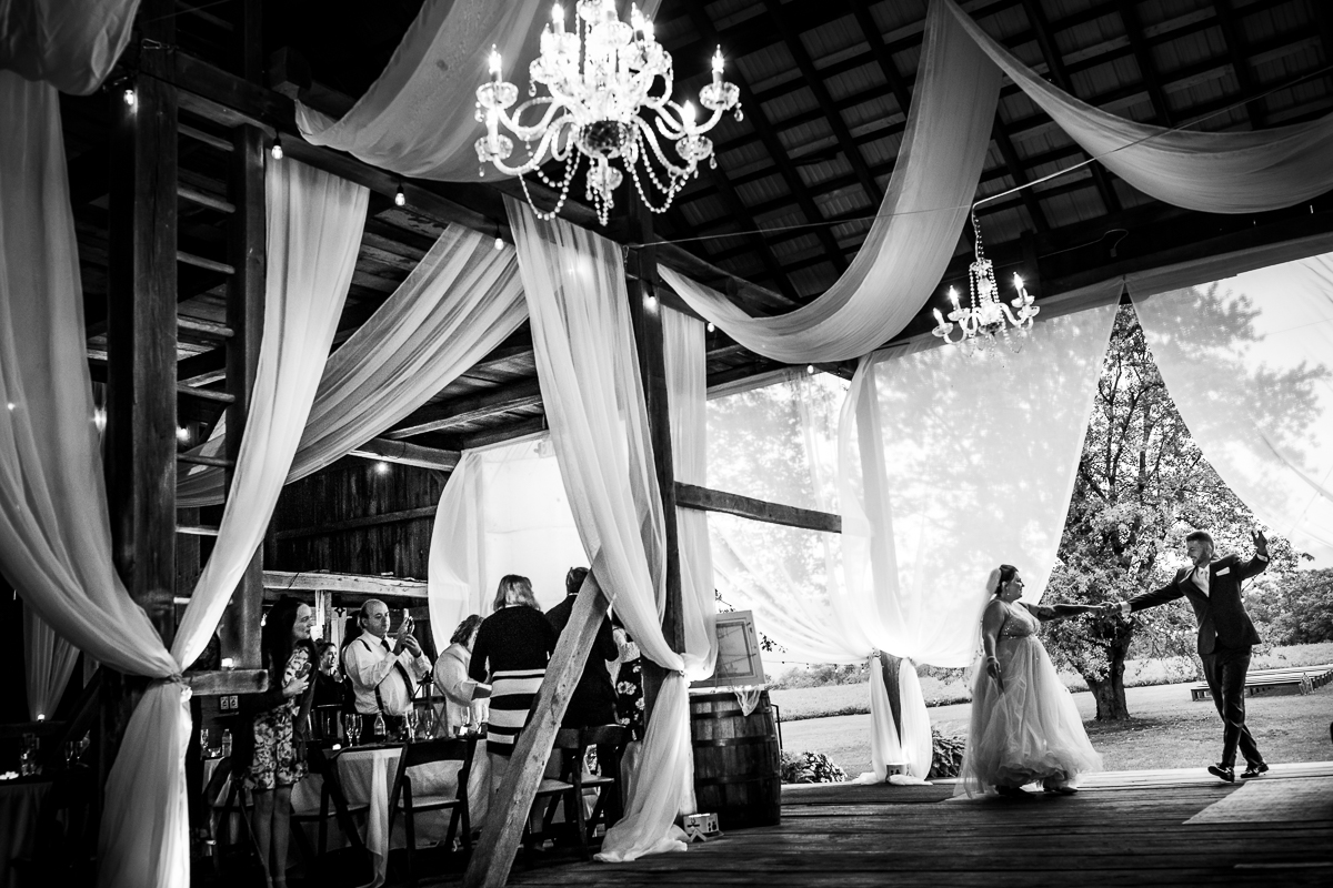 black and white photo heritage restored bride and groom entering reception space with guests clapping and cheering