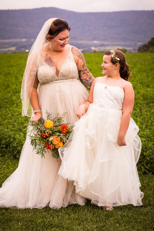 bride with groom's daughter smiling looking at each other holding bouquet outside