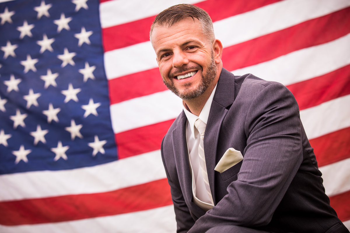 groom smiling at camera with American flag in background military wedding photographer