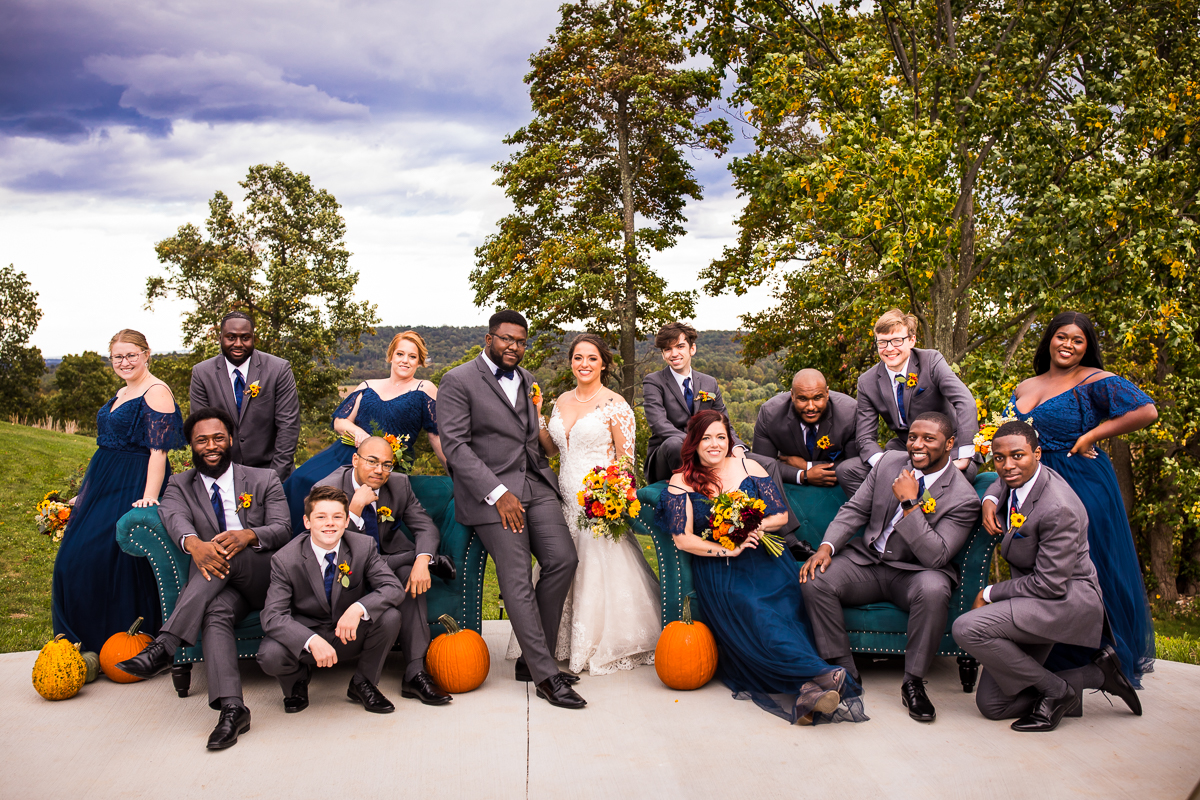 bride and groom posing with wedding party holding sunflower bouquets sitting with pumpkins 