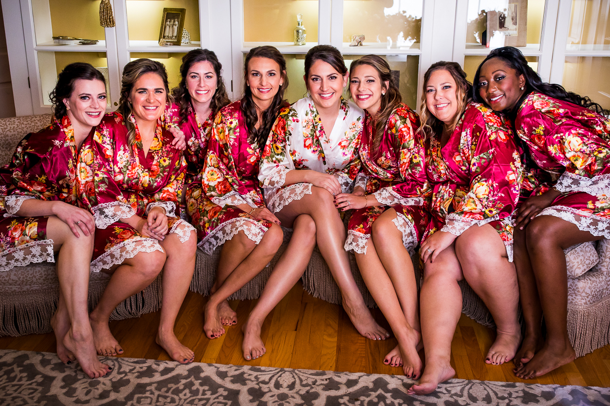 bride and bridesmaid sitting in bridal suite at Linwood estate in colorful floral robes smiling at camera