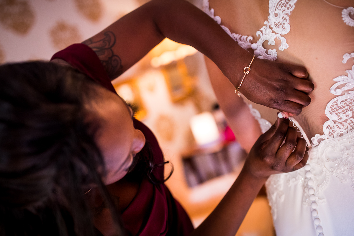 bridesmaid buttoning up bride's wedding dress