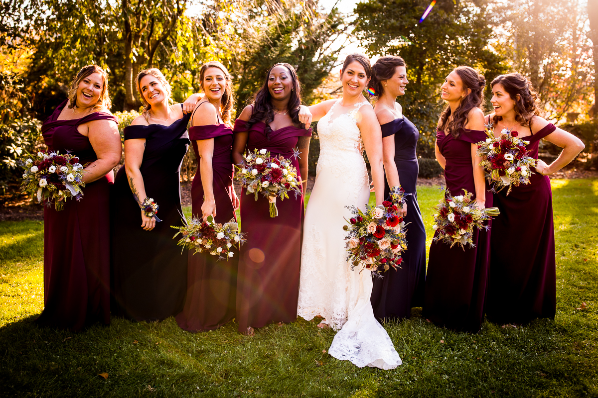 bride and bridesmaids posing outside with bouquets in hand smiling at the camera