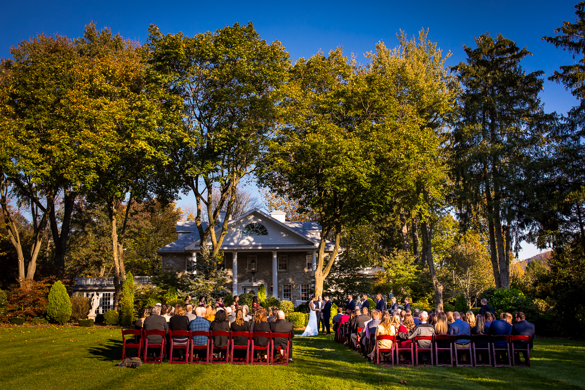 bride and groom holding hands during ceremony guests filling chairs outside Linwood estate wedding ceremony fall outdoors
