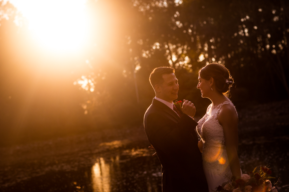bride and groom holding hands looking at each other smiling golden ray of sun in background 
