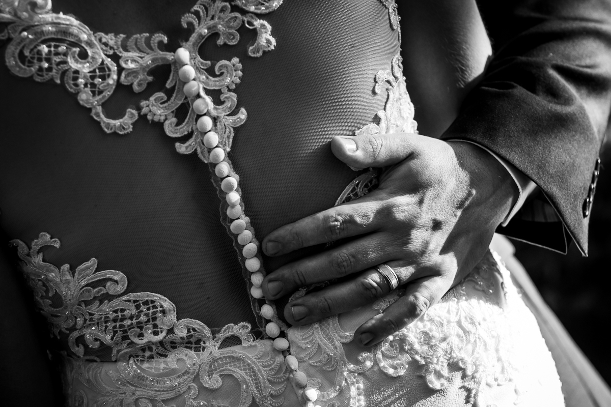 black and white photo of grooms hand around bride's waist with lace details and buttons visible on wedding dress