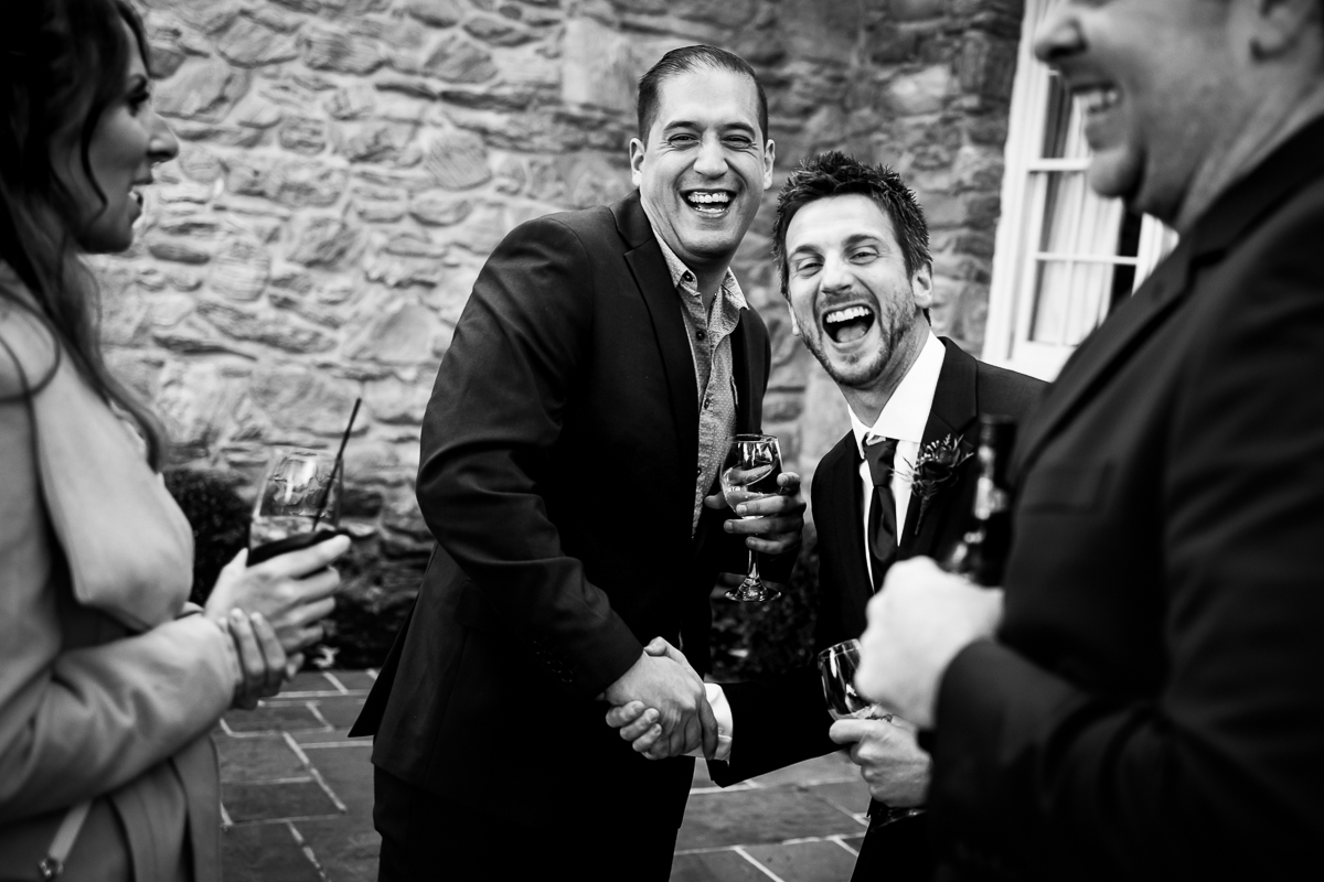 black and white photo of guest and groomsmen shaking hands laughing during cocktail hour 