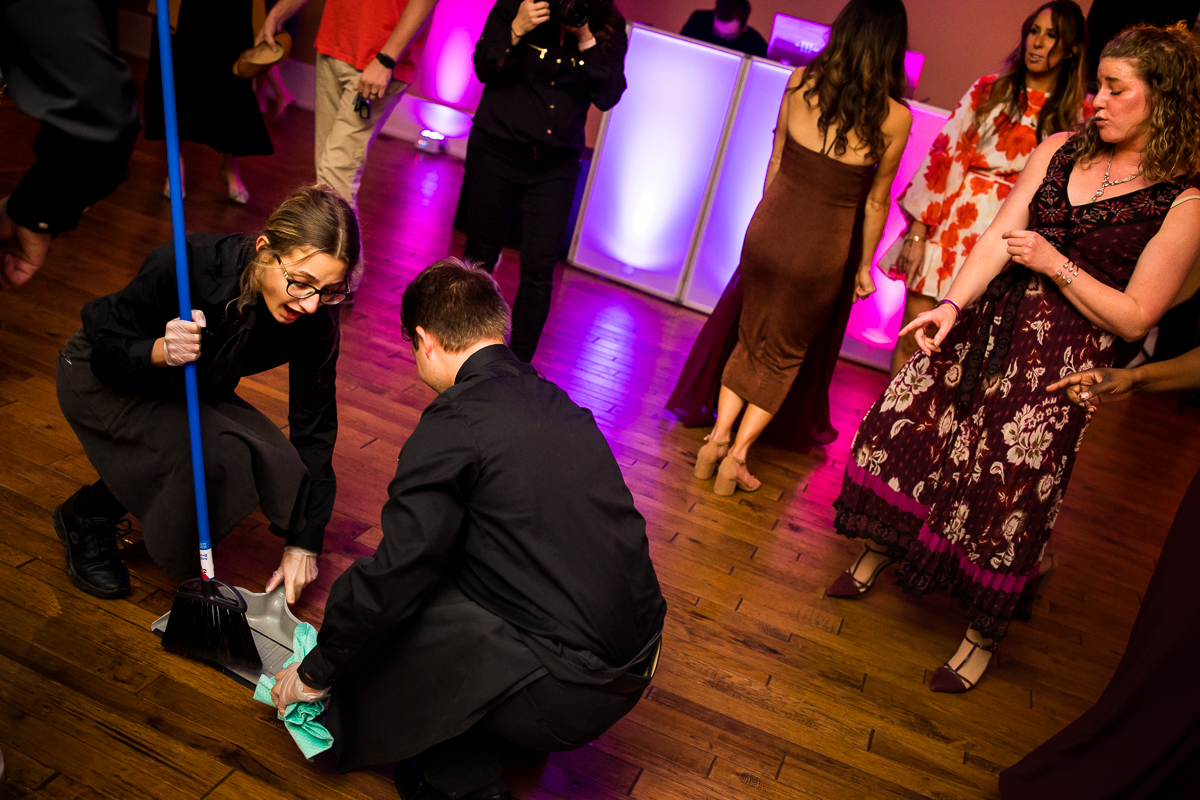 wedding staff cleaning up broken glass on dance floor during reception