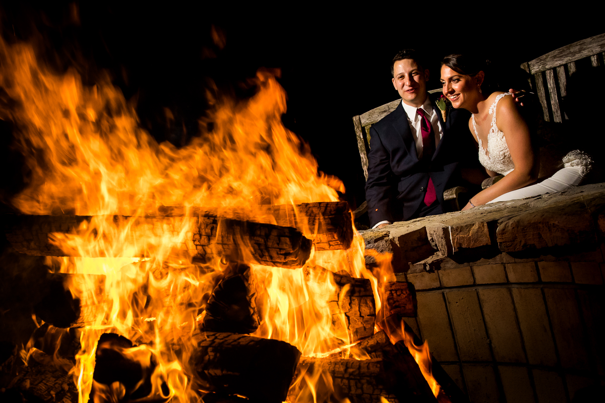 bride and groom sitting behind fire pit during wedding reception