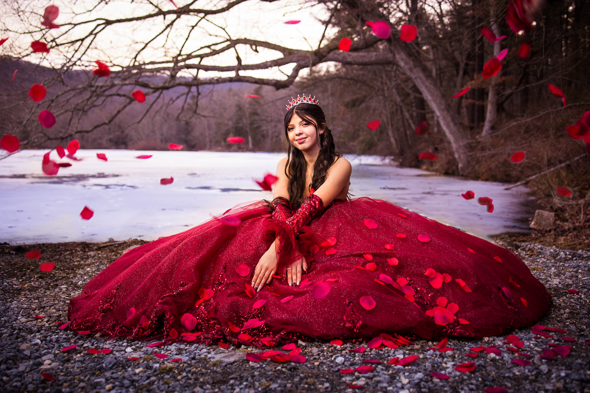 unique vibrant colorful central PA portrait photographer girl sitting on ground in snow with rose petals surrounding in red dress