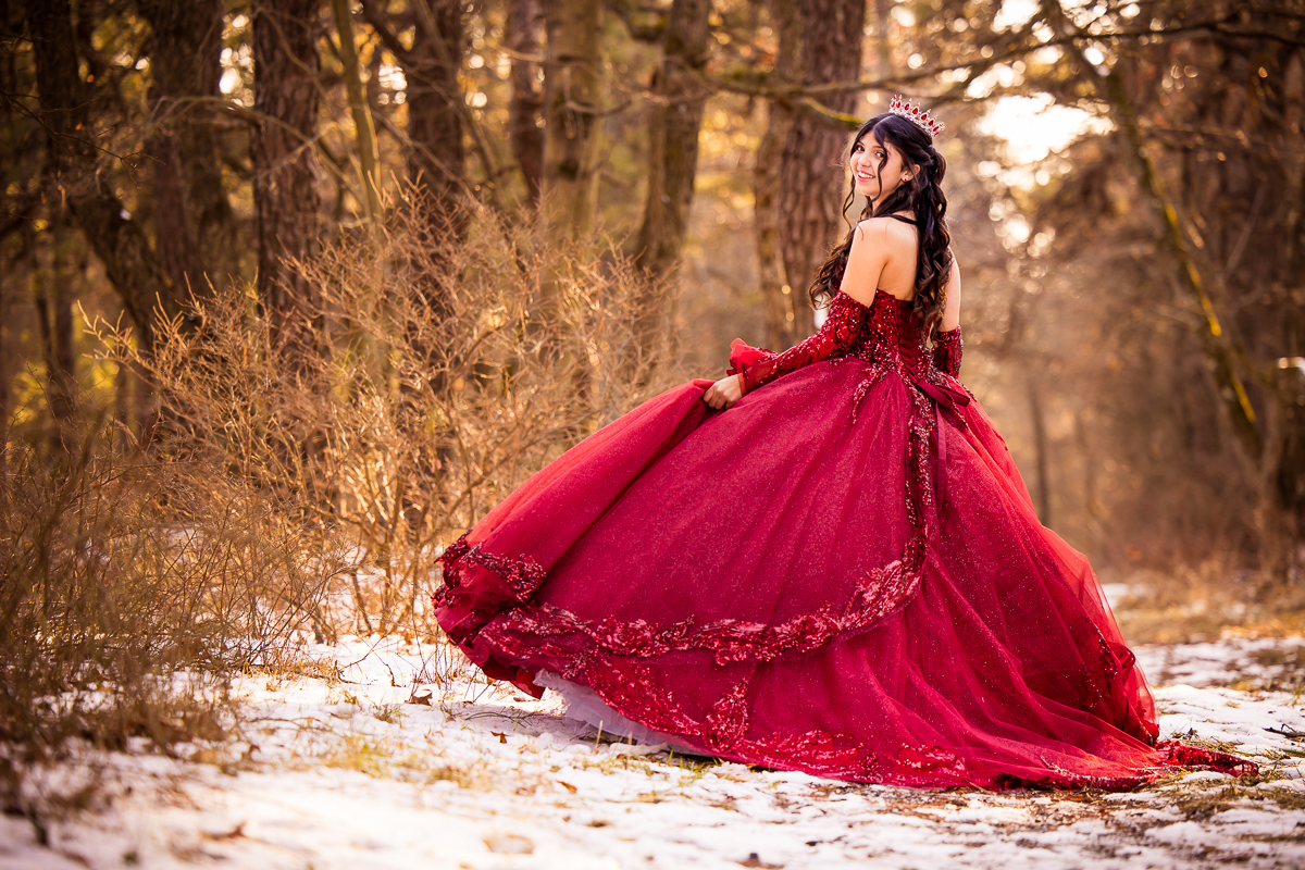 girl wearing red dress walking in woods with snow on ground looking back at camera smiling wearing crown