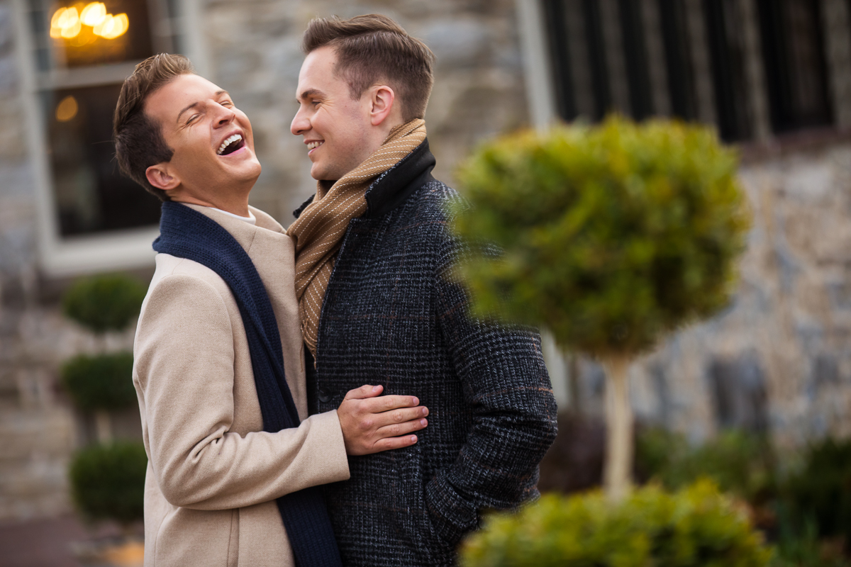 Couple standing outside of the Ashcombe Mansion laughing and smiling at each other in a candid photograph for their engagement session