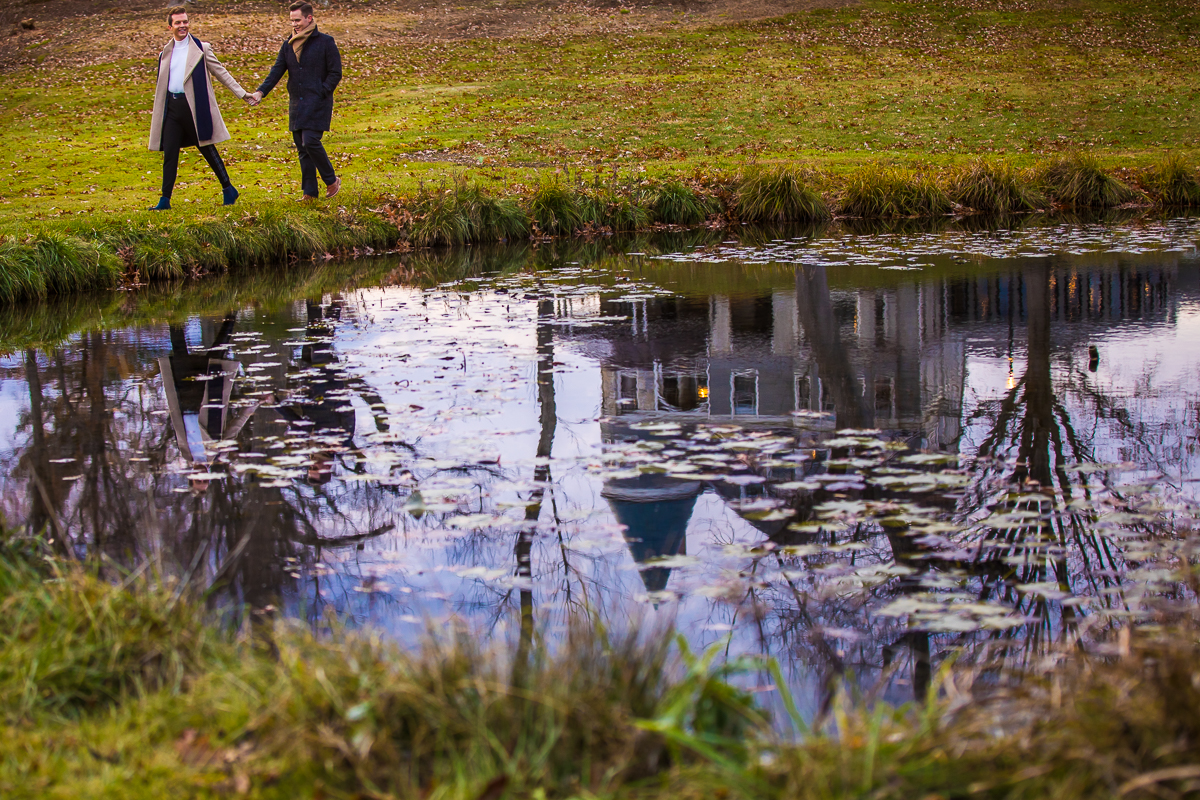 Gay couple walking around the pond outside for this Willows of Ashcombe Mansion engagement session using creative photography to capture the reflection of the mansion in the pond