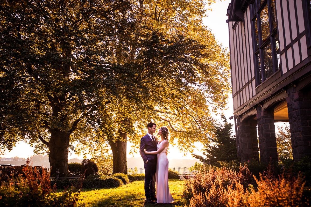 Couple standing outside of their Civic Club of Harrisburg Wedding venue backlit by the sunset, surrounded by trees