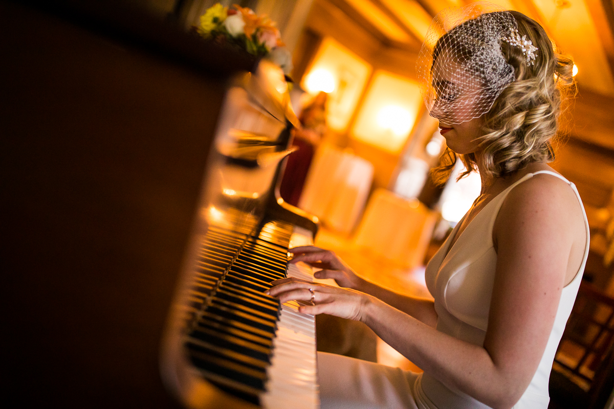 Photograph of the bride playing the piano in her wedding dress before the ceremony