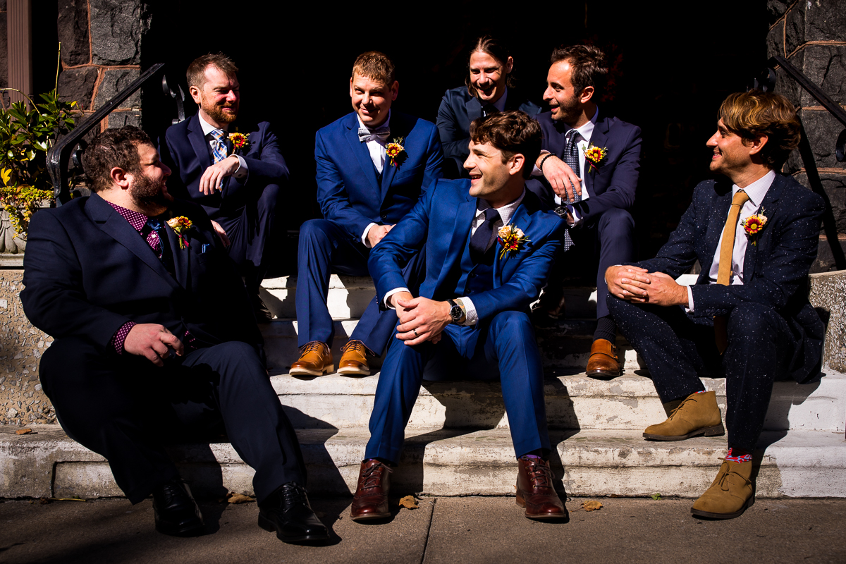 Candid photo of the groomsmen laughing and talking to each other outside of the Civic Club of Harrisburg in their navy blue tuxes before the wedding ceremony