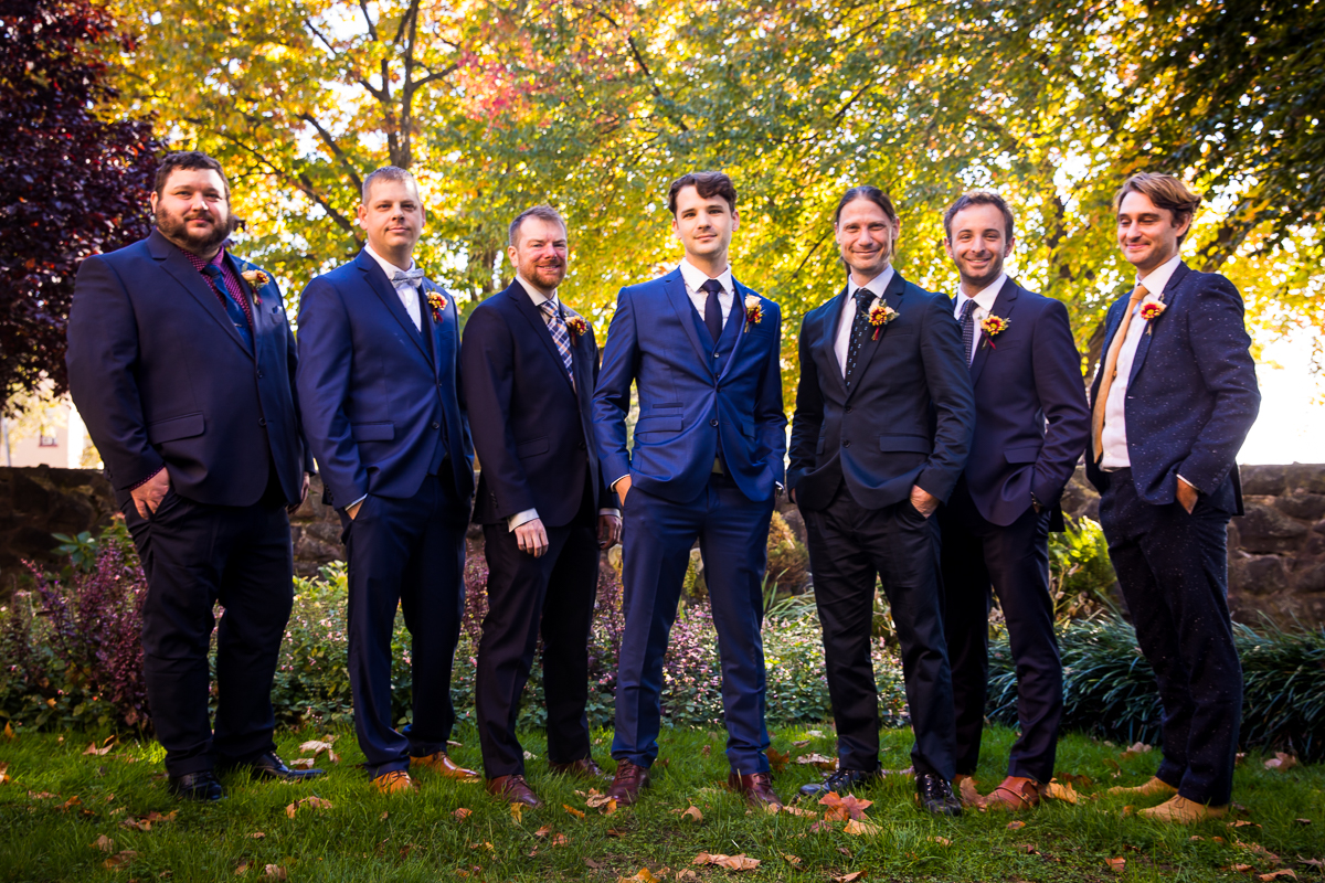 Traditional portrait of the groomsmen standing outside together in a line in their navy blue tuxes