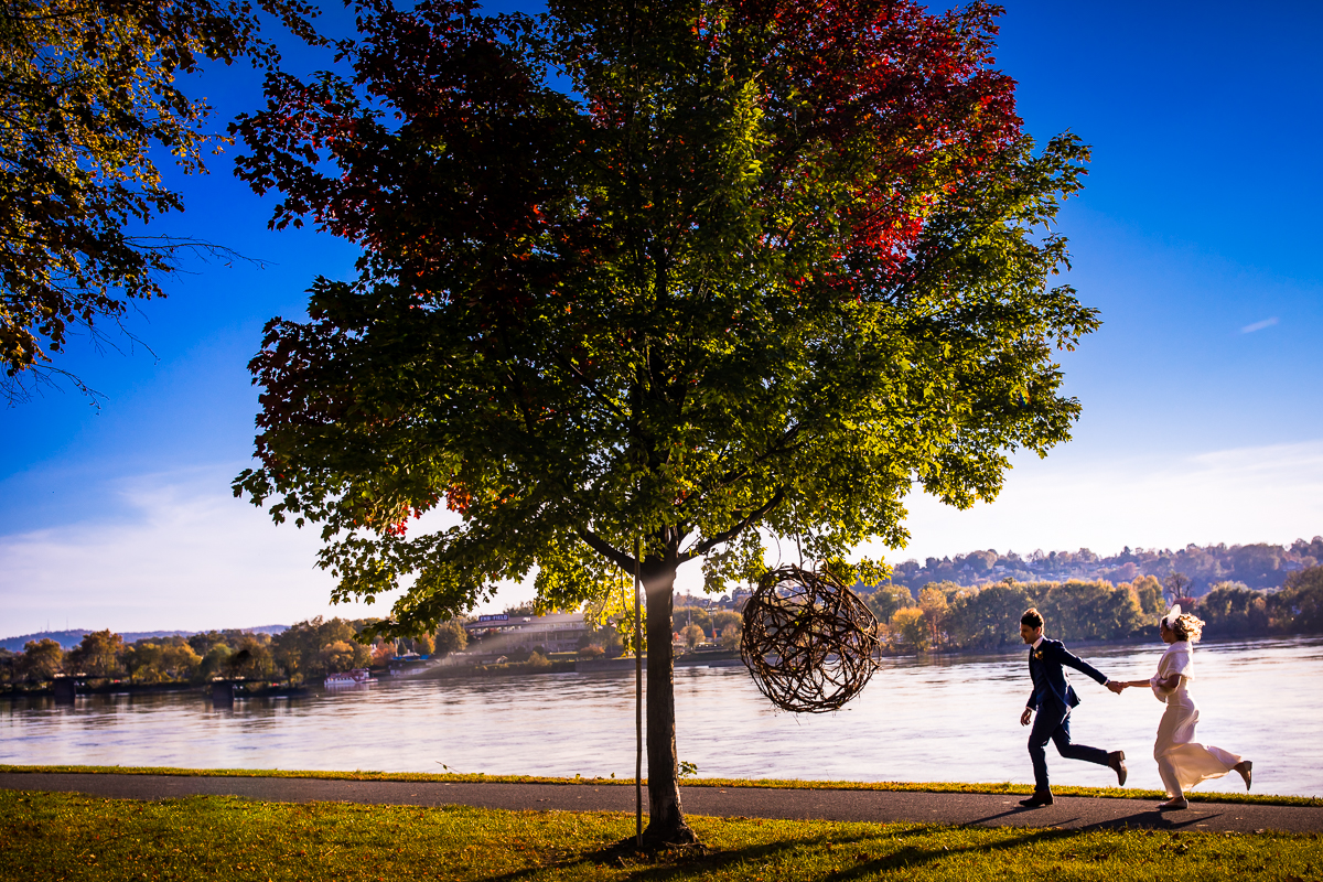 Colorful, vibrant photo of this couple running in front of the Susquehanna River on their wedding day holding hands