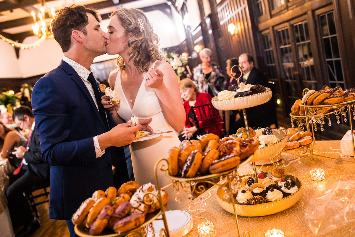 Image of the couple kissing in front of their dessert table inside of the Civic Club of Harrisburg for their wedding reception