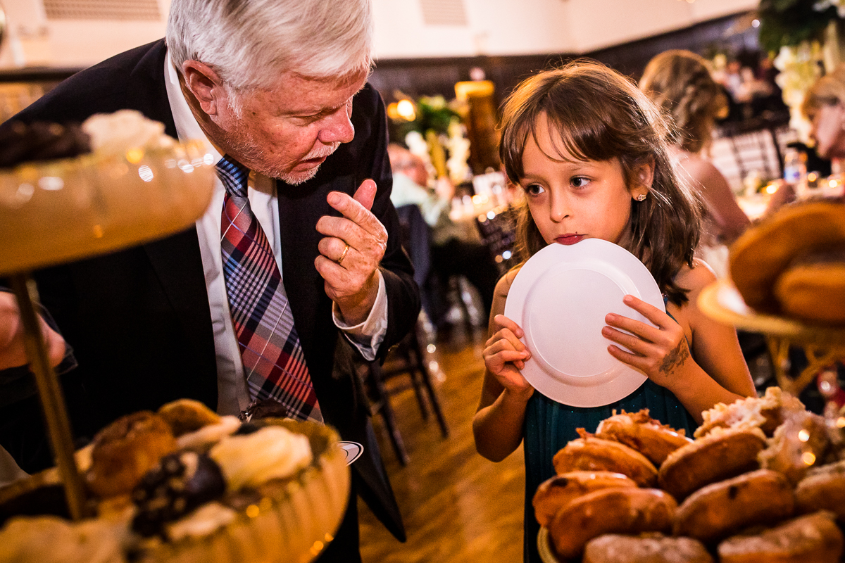 Image of an older man and a young girl holding her plate to her face debating on what desserts they want to eat first
