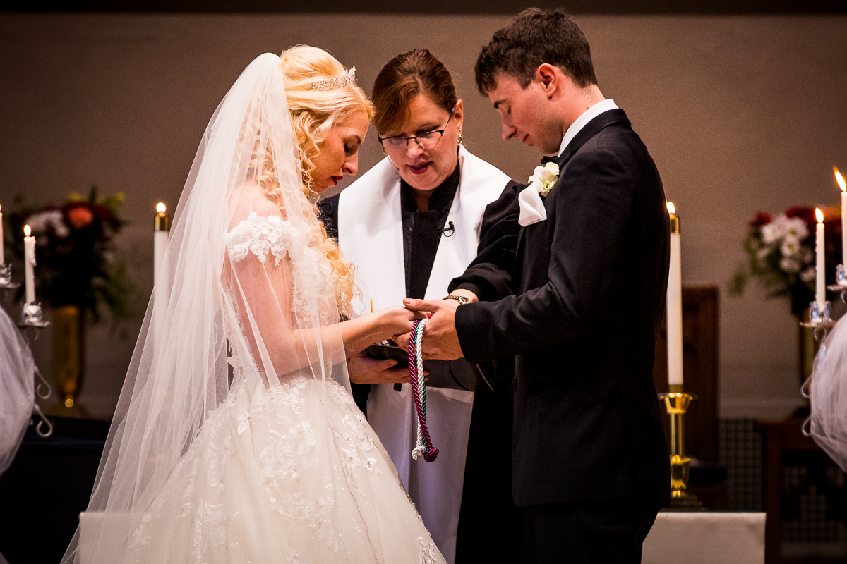Bride and Groom holding hands and colorful ropes praying during their wedding ceremony at First United Methodist Church in Hershey 