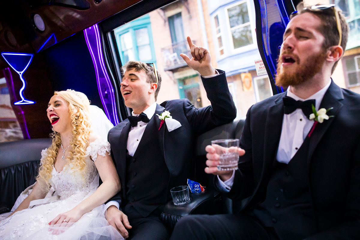 Photo of the Bride and Groom with a groomsman laughing and singing inside of a limo of their wedding day