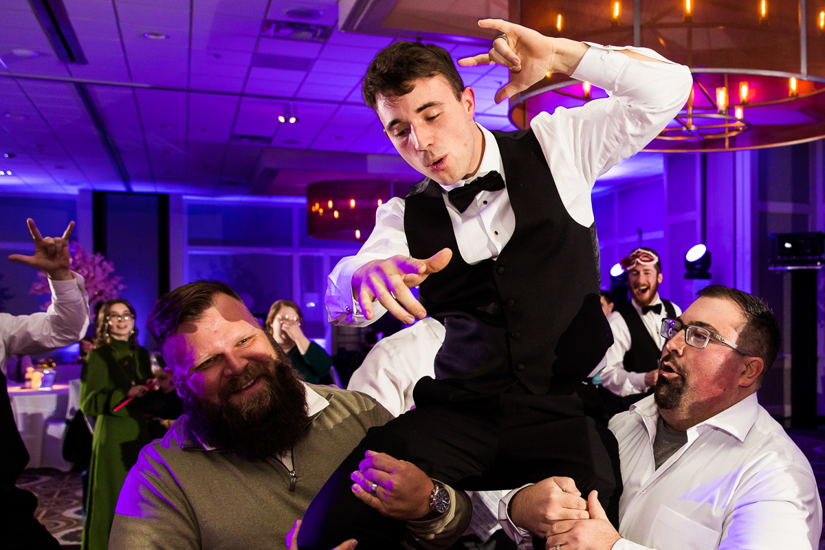 Colorful photo of guests lifting the groom up into the air while dancing during the wedding reception 