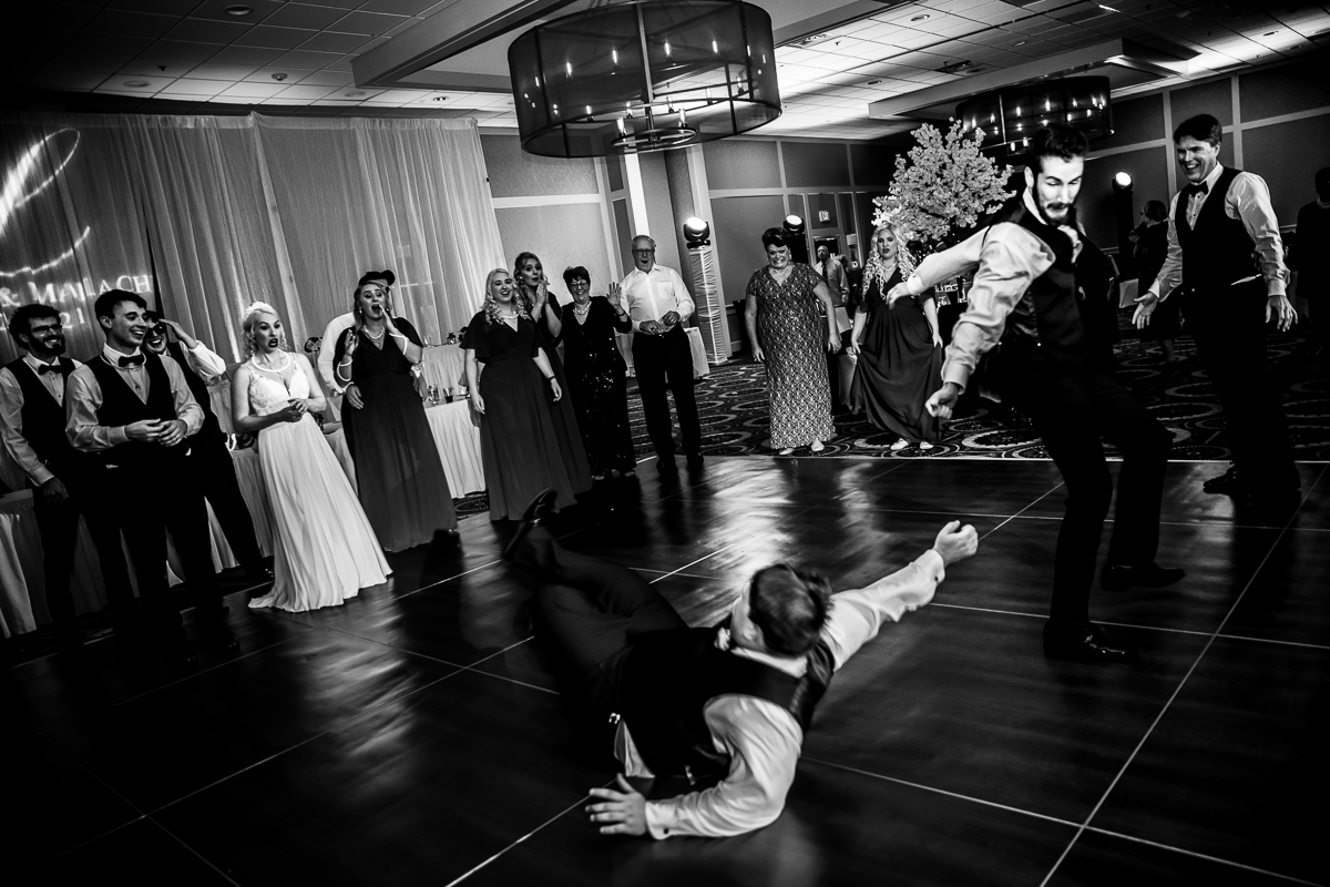 Black and white photo of guest dancing and falling with other guests looking shocked and laughing in the background during the wedding reception at Best Western Harrisburg 