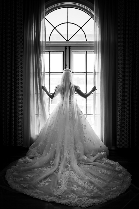 Black and white photo of bride in her wedding dress holding the curtains looking out the window of the King Mansion Harrisburg Wedding