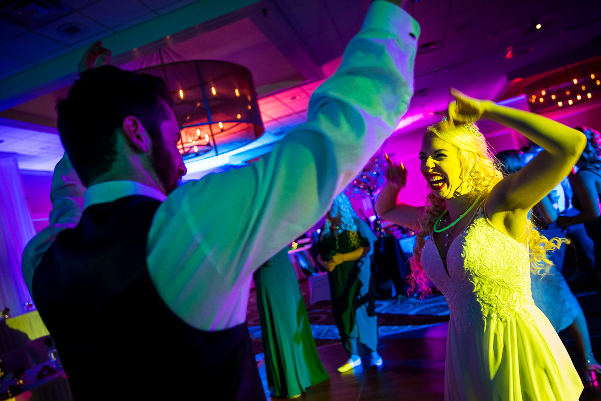 Colorful and vibrant photo of bride and guests dancing together with glow sticks and laughing during the wedding reception