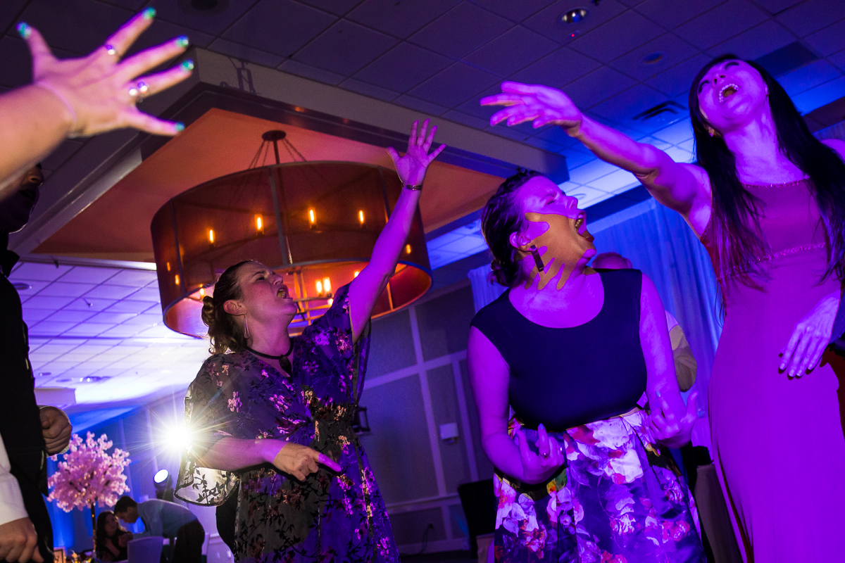 Colorful and vibrant photo of guests singing with their hands in the air during the wedding reception