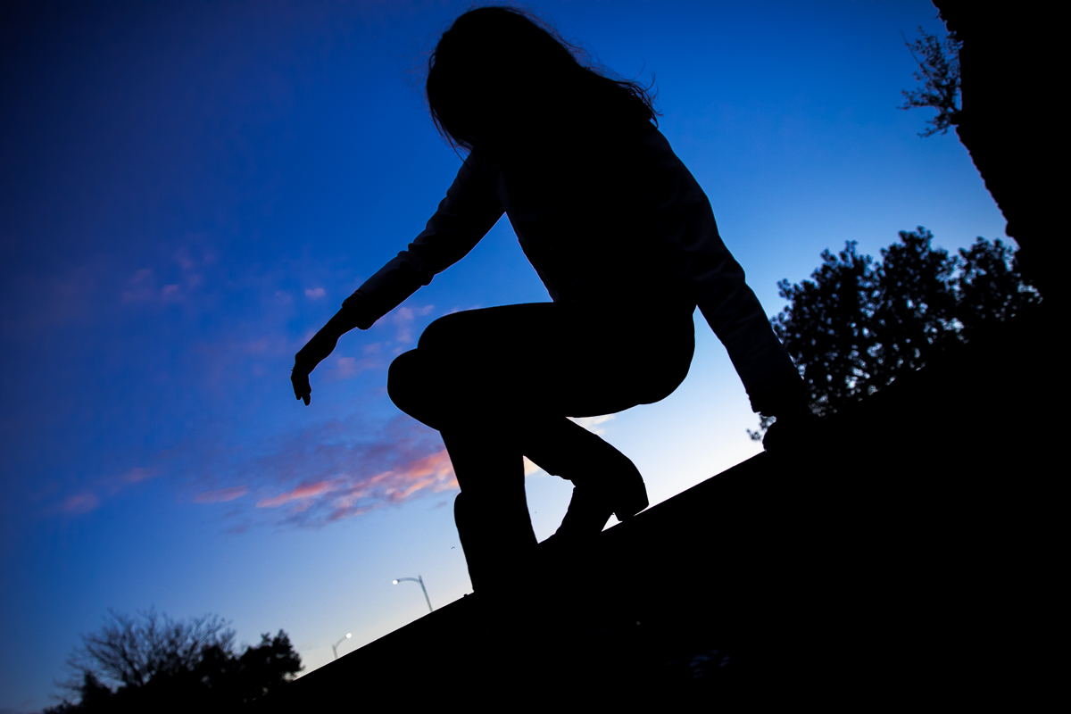 vibrant, unique image of a girl sitting on a wall with one hand above her knees with the sun setting behind her in this arts quest photographer image by lisa rhinehart