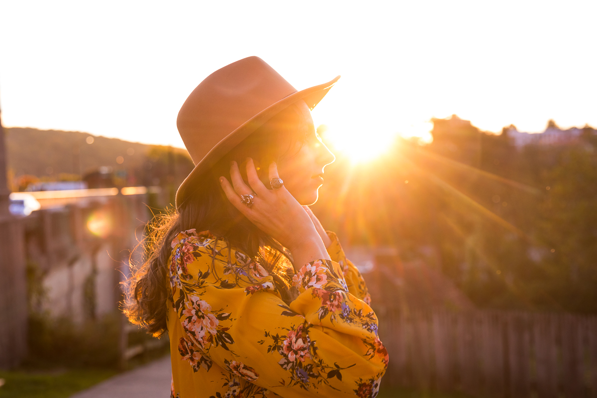 Sunset photo of girl playing with her hair with a bright yellow floral shirt and tan hat on taken by Creative Branding Photographer, lisa rhinehart
