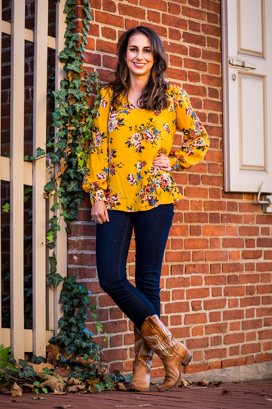 vibrant photo of lauren in a bright yellow floral shirt with cowgirl boots standing against a brick wall with a vine coming down the wall in bethleham, pa