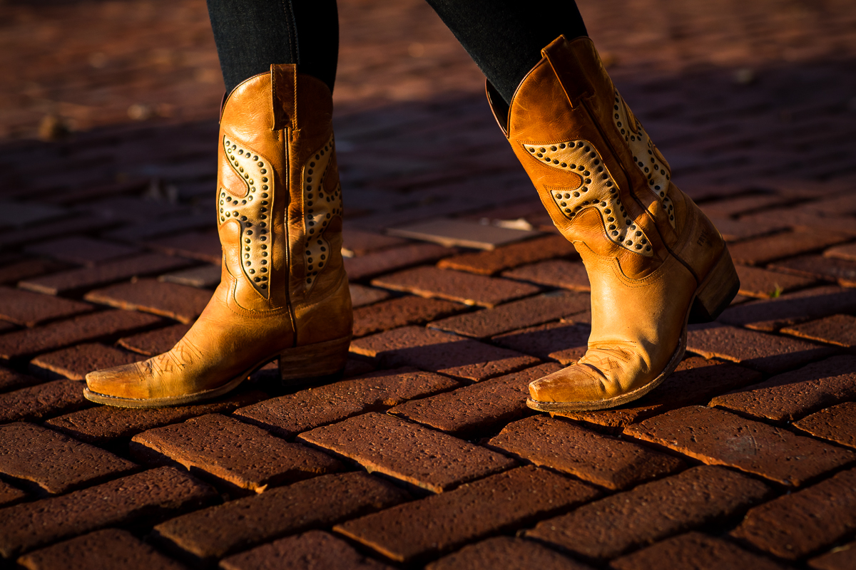 Brown cowgirl boots with a unqiue pattern on them walking across red bricks in the sunset taken by bethleham portrait photographer lisa rhinehart